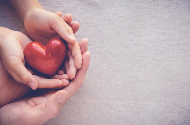 Hands of child and adult holding a red heart